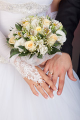 Obraz na płótnie Canvas Bride and groom hands with wedding rings and bouquet of roses