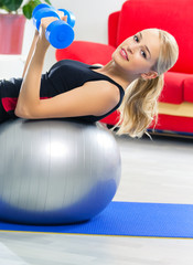 Woman exercising with dumbbell on fit ball, at home