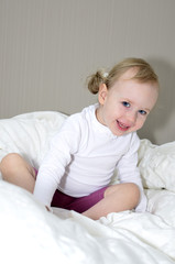 Fototapeta premium little girl sitting on a bed and smiling