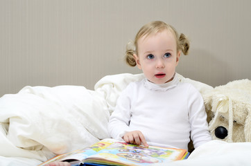 little girl sitting on the bed and reading a book