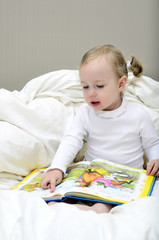 little girl sitting on the bed and reading a book