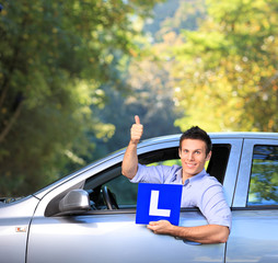 Happy male in his car holding a  L sign and giving thumb up