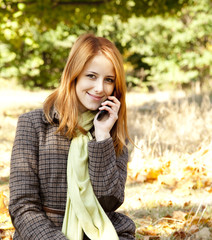 Red-haired girl calling by the phone in the autumn park.