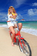Obraz na płótnie Canvas 波打ち際で自転車に乗りオレンジジュースを持っている女性