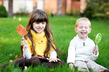 Little friends eating lollipops together on a lawn