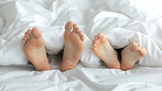 Feet of playful couple spending time in bed