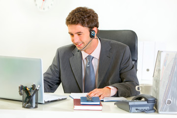 Smiling modern manager with headset looking in laptop