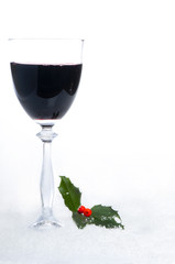 Glass of red wine with holly in the snow