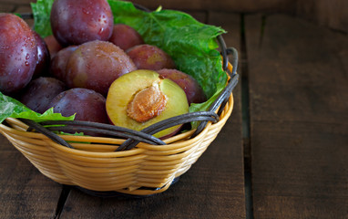 Basket of fresh plums on old wooden table