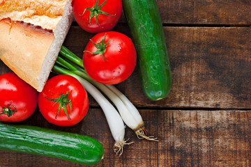 Tomatoes, cucumber, bread and spring onions on old wooden table