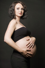 Young pregnant woman posing on black background.