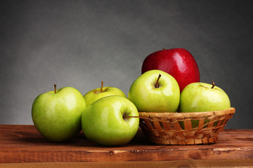 juicy sweet apples in basket on wooden table on gray background