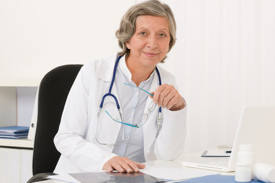 Senior doctor female sit behind office desk