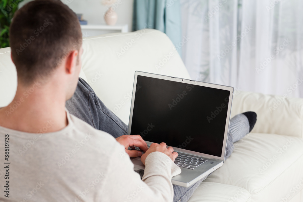 Poster man lying on his couch to use a laptop