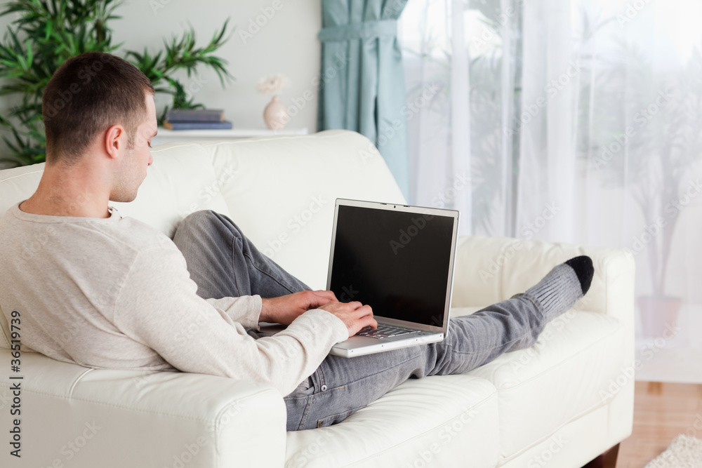Poster man lying on his couch using a laptop