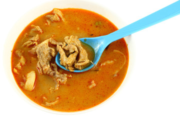 Pork spicy curry with blue spoon on white background.
