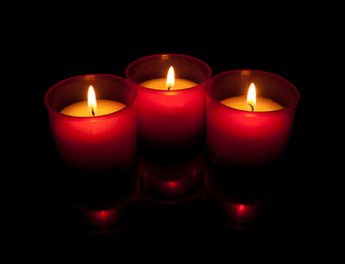 Fototapeta na wymiar Trzy wotywne świece w czerwonym posiadaczy ponad czarny