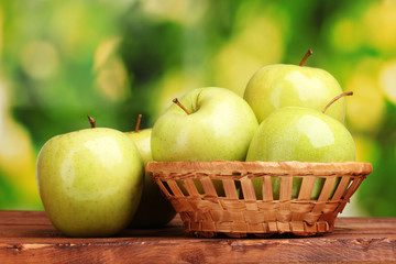 juicy green apples in basket on wooden table on green background