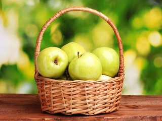 juicy green apples in basket on wooden table on green background