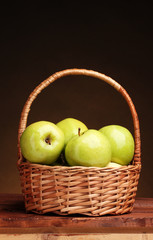 juicy green apples in basket on wooden table on brown background