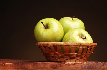juicy green apples in basket on wooden table on brown background