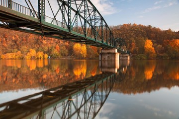 Metal bridge connecting river banks with reflection in autumn