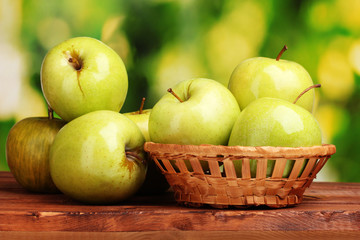 juicy green apples in basket on wooden table on green background