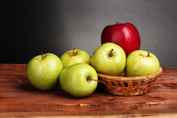 juicy sweet apples in basket on wooden table on gray background
