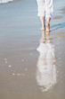 Frau im weißen Sommeroutfit spaziert am Strand
