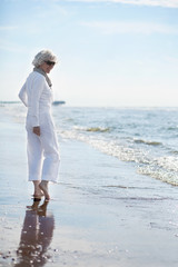 attraktive, grauhaarige Frau genießt Spaziergang am Meer