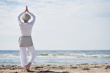 Fototapeta na wymiar Aktywny starszy kobieta robi joga na plaży