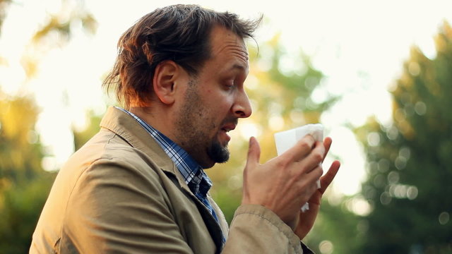 Sick man blowing his nose into tissue, outdoors