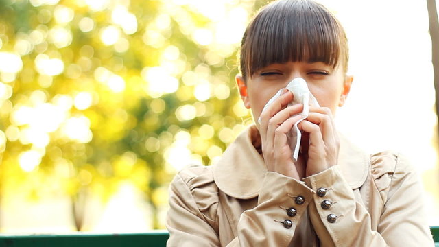 Sick woman blowing his nose into tissue, outdoors