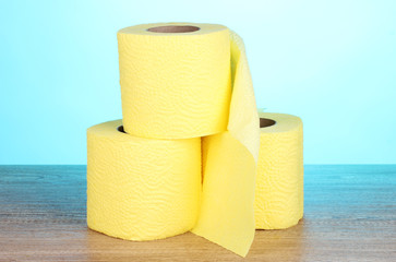 three rolls of toilet paper on wooden table on blue background