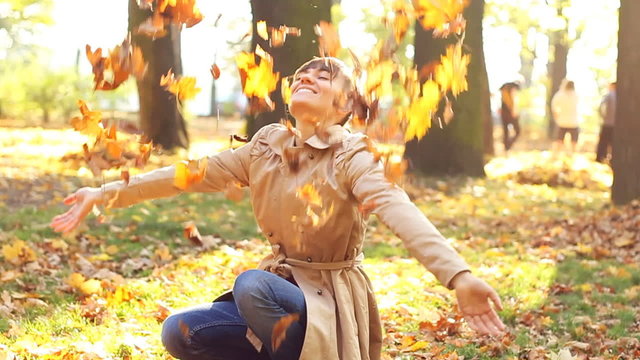 Young happy woman throwing golden leaves in the air, slow motion