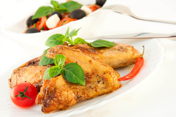 Chicken wings a grill with a tomato and a basil.