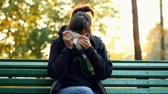 Sick woman blowing his nose into tissue, outdoors