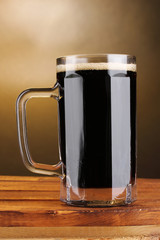 dark beer in a mug on wooden table on brown background