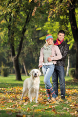 Naklejka na ściany i meble A smiling couple and their dog posing in the park
