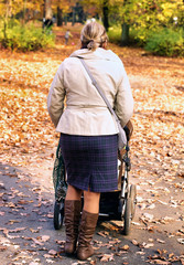 Mother with pram walking in an autumn park