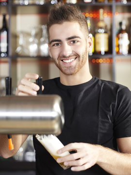 Handsome young barkeeper is tapping a beer in a pub