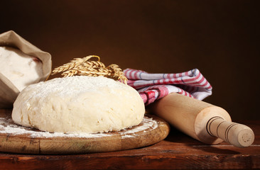 Dough and bags with flour on wooden table on brown background