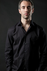 Man posing in black shirt on dark background in studio.