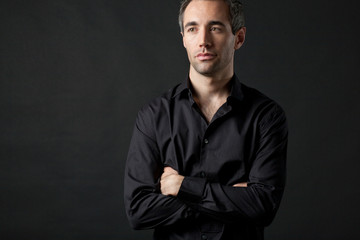 Man posing in black shirt on dark background in studio.