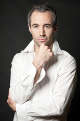 Man posing in white shirt on dark background in studio.