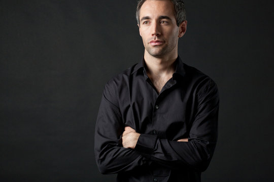 Man posing in black shirt on dark background in studio.