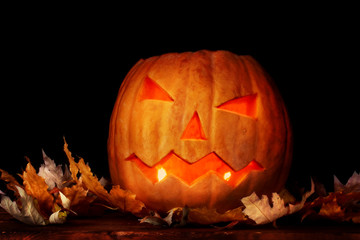 Halloween Pumpkin and autumn leaves on wooden table in dark