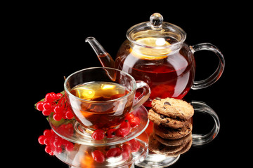 Glass teapot and cup with black fruit tea and cookies isolated