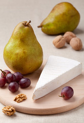 Green pears, cheese brie, walnuts and grapes on wooden board