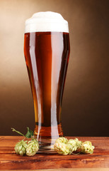 beer in glass and green hop on wooden table on brown background